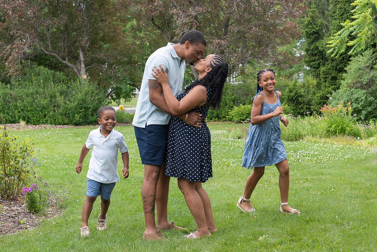 Parents kiss while their children laugh and play during a summer garden family session in Edmonton