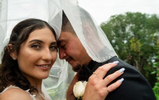 A bride looking towards the camera while her groom embraces her with his head bowed and eyes closed during their wedding ceremony.