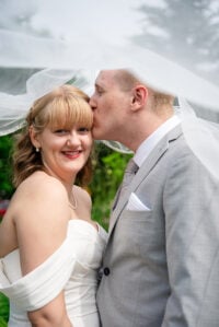 Side profile of the groom kissing his smiling bride as her veil flows during an Edmonton wedding