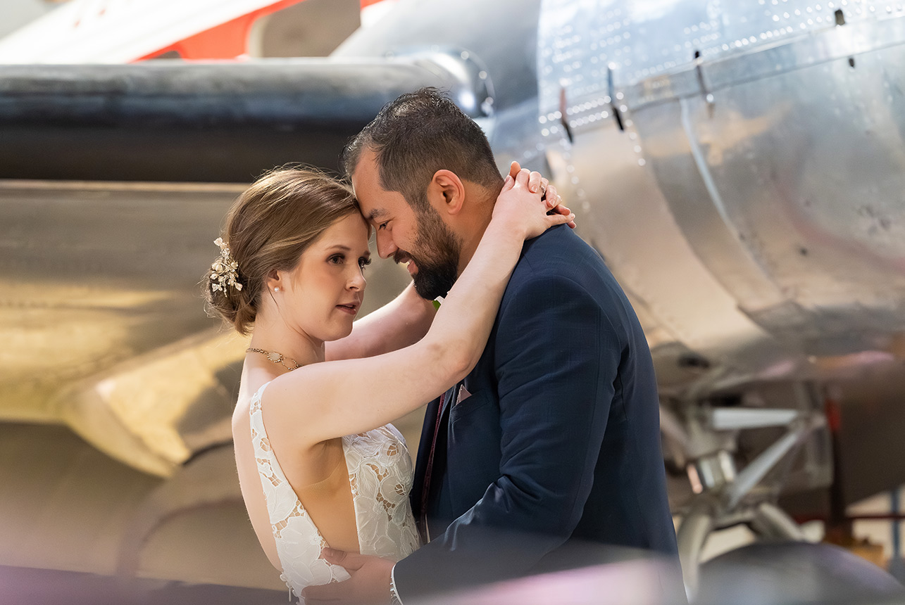 Bride and groom embrace in a softly lit portrait with an elegant aircraft backdrop