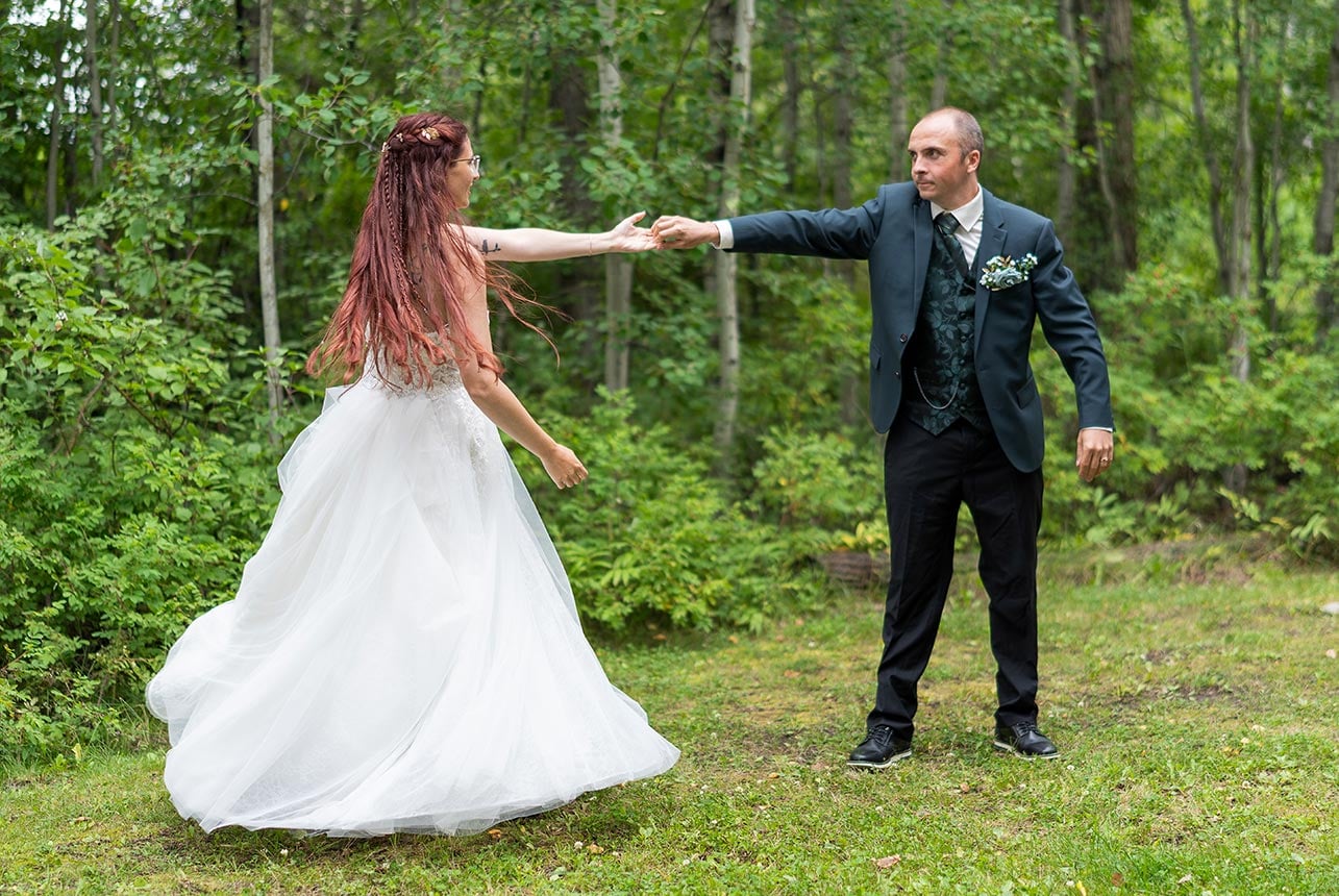Bride twirls as her partner reaches for her hand in a forest clearing, dress flowing in motion