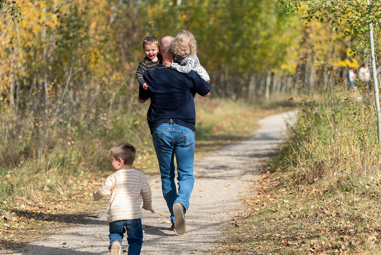 Grandfather carrying two toddlers along a trail during a candid family photography session near Edmonton
