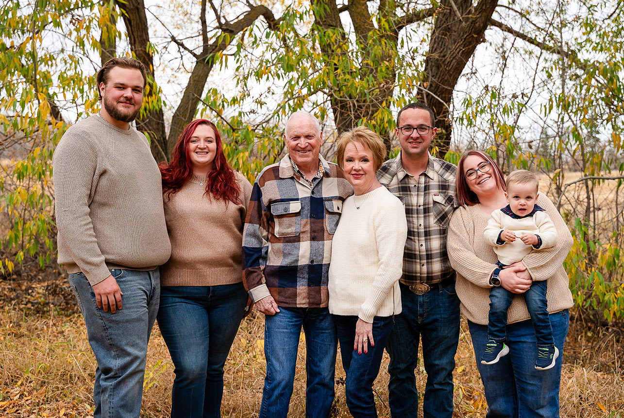 Multi generational family portrait with grandparents, adult children, and a young child outdoors in fall