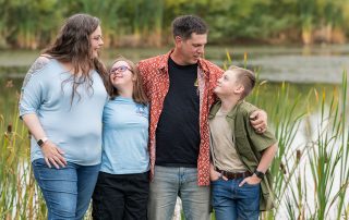 Family of four sharing a relaxed moment beside a pond during a family session in the Edmonton area