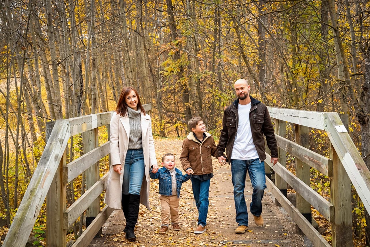 Family of four walking together on an autumn bridge during a relaxed outdoor family photography session in Edmonton