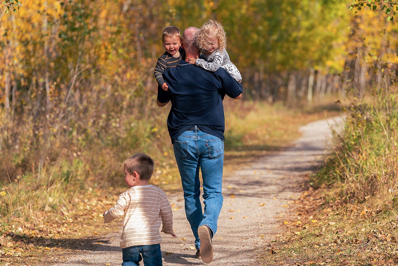 Grandfather walking with three grandchildren along an autumn park path near Edmonton, photographed by Catriona Hope Photography.