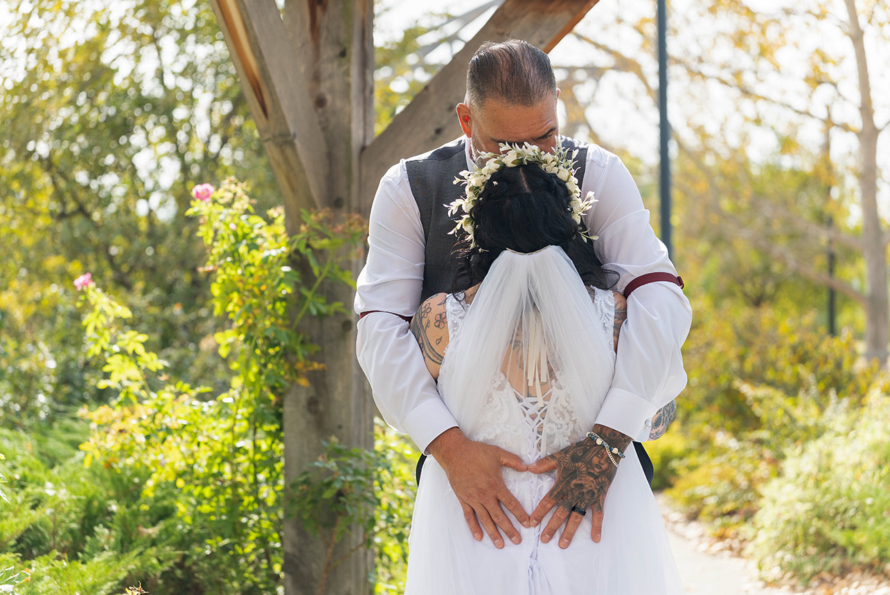 Trudy and Byron sharing a quiet portrait moment beneath the wooden structure at Stone Barn Garden.
