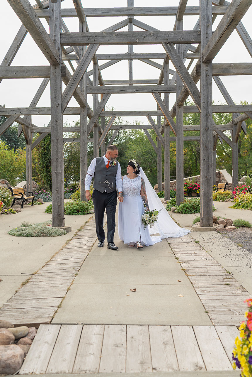 Trudy and Byron walking together through Stone Barn Garden and Cultural Village for their wedding portraits in Leduc.