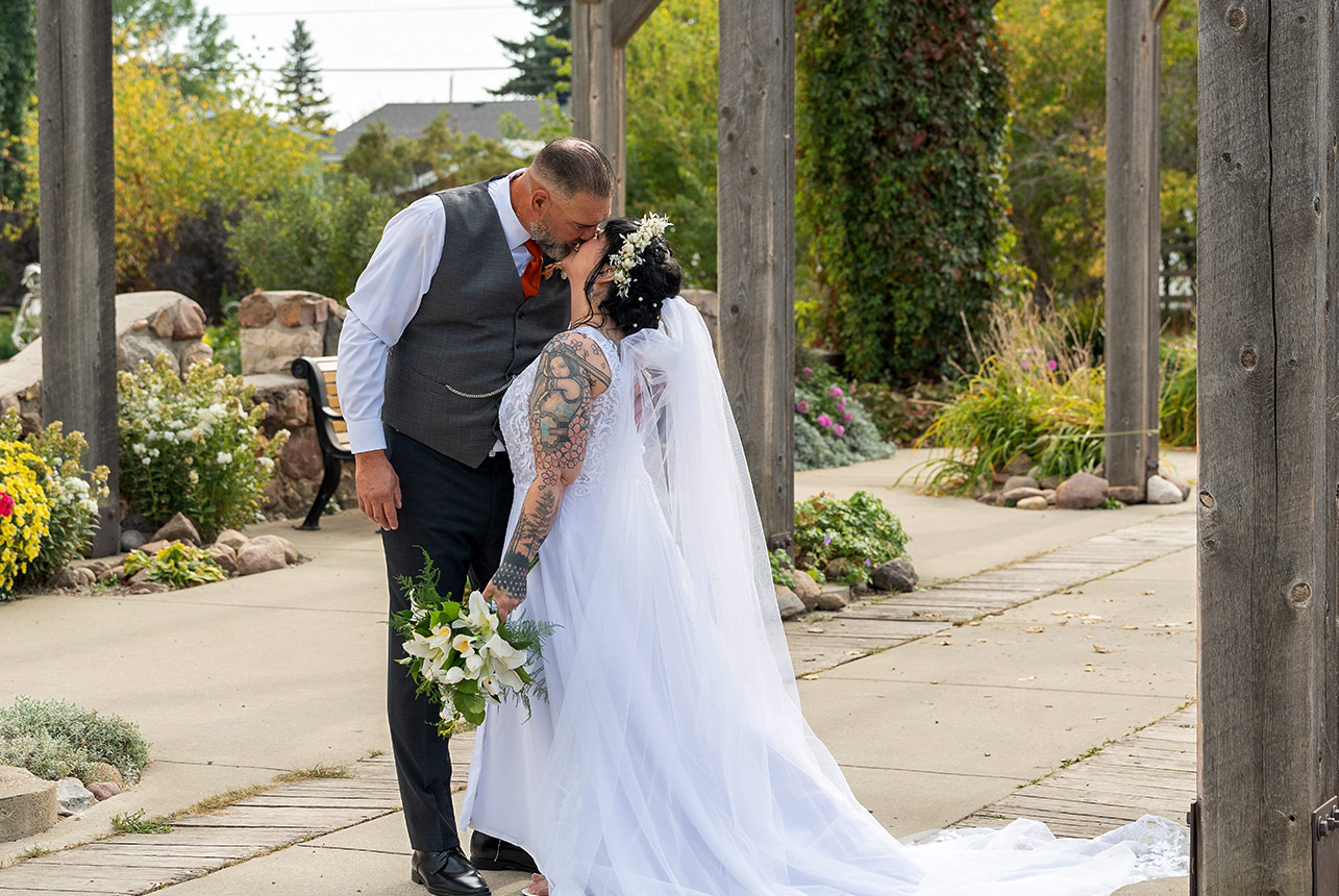 Trudy and Byron sharing a kiss during their wedding portraits at Stone Barn Garden in Leduc.